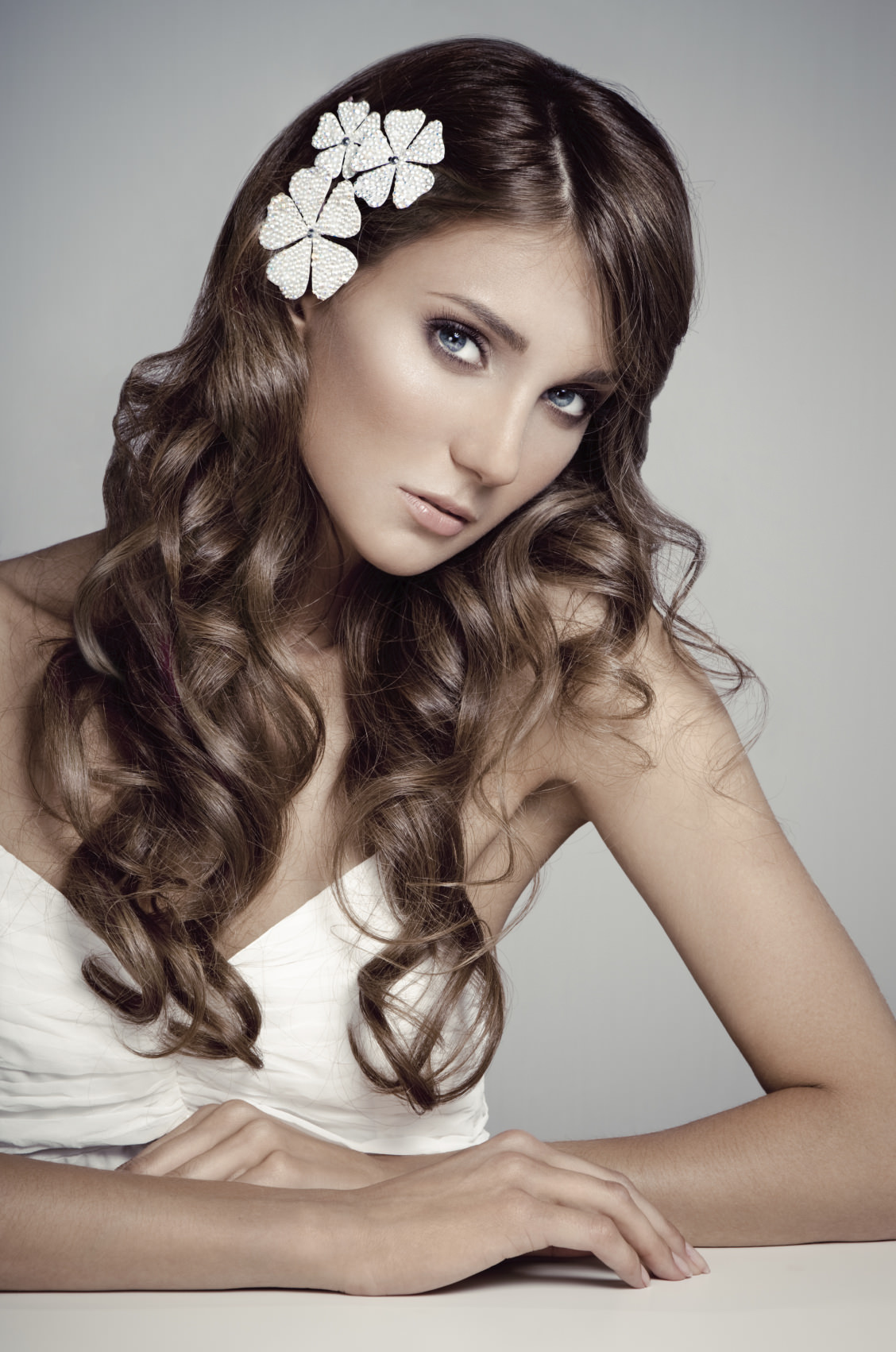Beauty portrait of young fashion model wearing hair accessory, looking at camera. Professional make-up and hairstyle, gray background